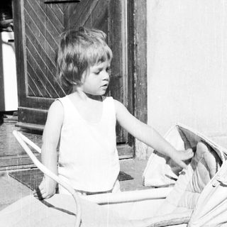Boy sits in a toy car outside a door.