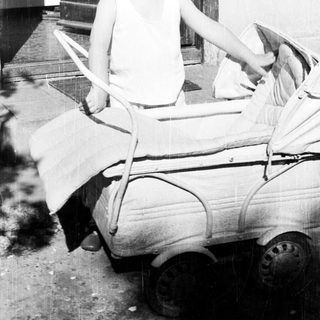 Boy sits in a toy car outside a door.