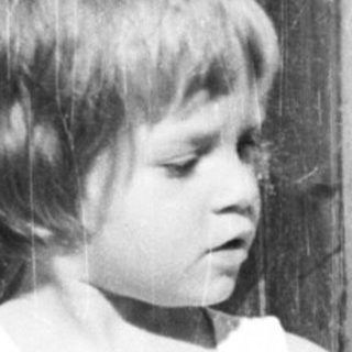 Boy sits in a toy car outside a door.