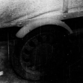 Boy sits in a toy car outside a door.