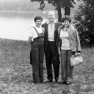 Three people stand outdoors near a body of water.
