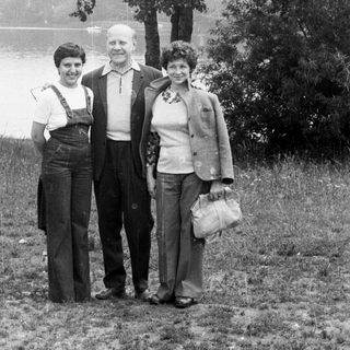 Three people stand outdoors near a body of water.