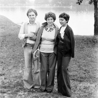 Three people stand near a body of water, in a field.