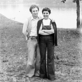 Couple posing outdoors, wearing 1970s style clothing.