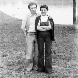 Couple posing outdoors, wearing 1970s style clothing.