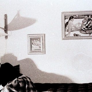 Person writing in bed, with artwork and lamp visible.
