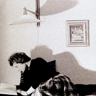 Person writing in bed, with artwork and lamp visible.
