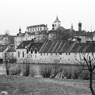 Historic castle complex sits beside a river, viewed from afar.