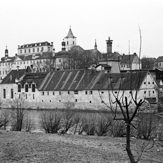Historic castle complex sits beside a river, viewed from afar.