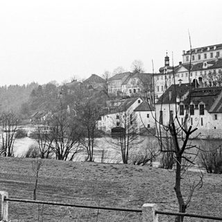 Black and white photo shows a town alongside a river.
