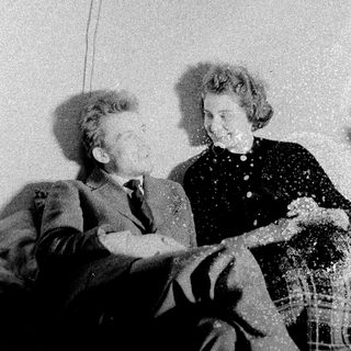Here's a brief summary of the image: Man and woman seated, smiling, in a vintage interior.