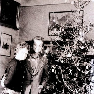Couple stands near a small, decorated Christmas tree.