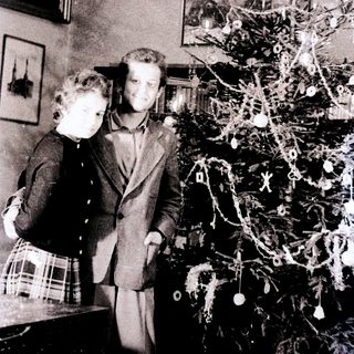 Couple stands near a small, decorated Christmas tree.