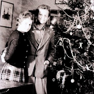 Couple stands near a small, decorated Christmas tree.