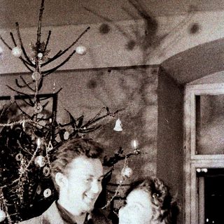 Couple stands near decorated Christmas tree in vintage setting.