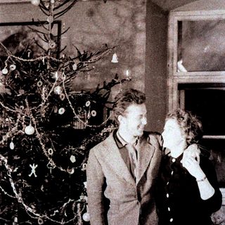 Couple stands near a sparsely decorated Christmas tree.
