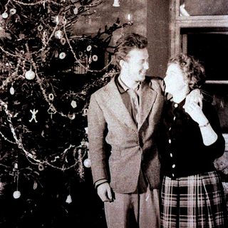 Couple stands near a sparsely decorated Christmas tree.