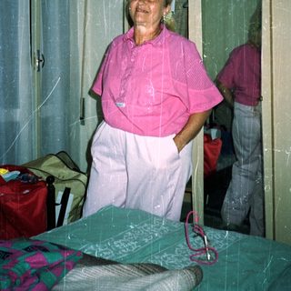 Woman in pink shirt and pants stands in a bedroom.