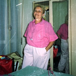 Woman in pink shirt and pants stands in a bedroom.