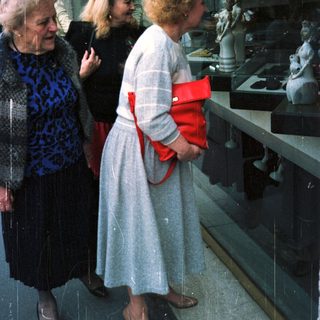 Three women view statues displayed in a shop window.