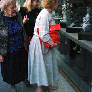 Three women view statues displayed in a shop window.