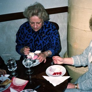 Two women sit at a table, eating cake.