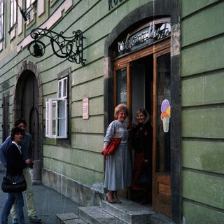 People stand near a building with a storefront and sign.