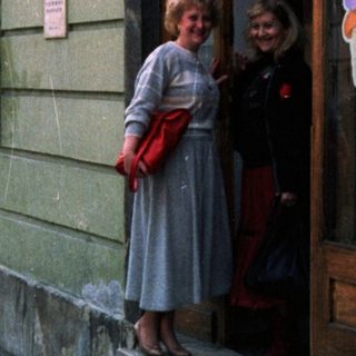 People stand near a building with a storefront and sign.