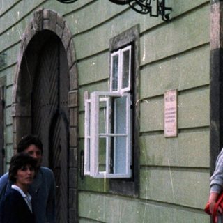 People stand near a building with a storefront and sign.