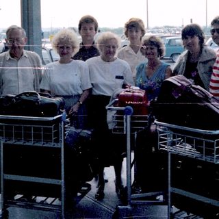 Group portrait near airport, luggage carts visible.