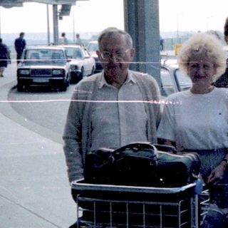 Group portrait near airport, luggage carts visible.
