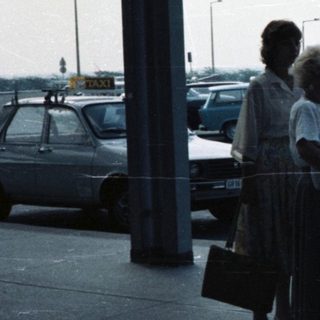Group standing near luggage carts under airport shelter.