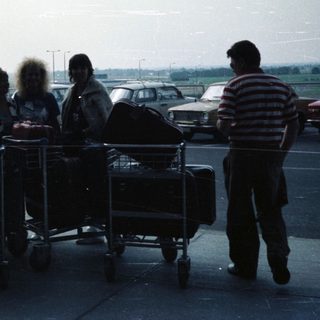 Group standing near luggage carts under airport shelter.