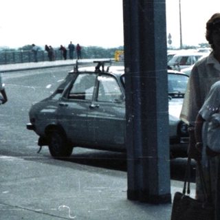 Group of people and luggage stand under an airport canopy.