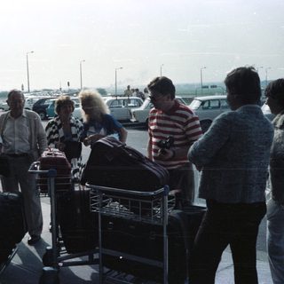 Group with luggage waits outside an airport terminal.