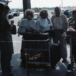 Group with luggage waits outside an airport terminal.
