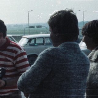 Group with luggage waits outside an airport terminal.