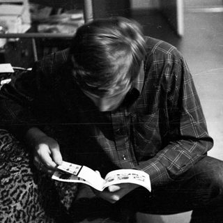 Person kneeling, reading a booklet while seated on a surface.