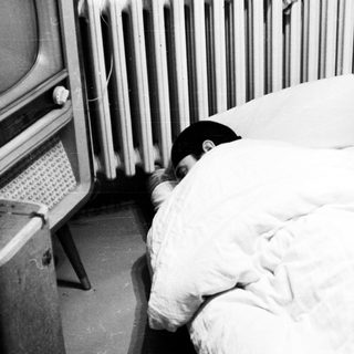 Person sleeping under a blanket near a radiator and TV.