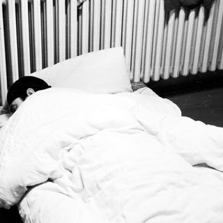 Person sleeping under a blanket near a radiator and TV.