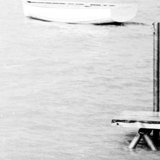 Child entering water near a dock, black and white.