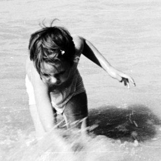 Child entering water near a dock, black and white.