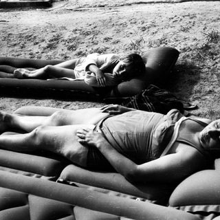 Here's a brief summary of the image: Two people lie relaxed on inflatable mattresses outdoors.