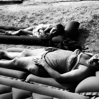 Here's a brief summary of the image: Two people lie relaxed on inflatable mattresses outdoors.