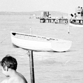Boy sits on a pier overlooking a body of water.