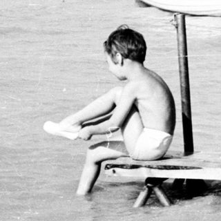 Boy sits on a pier overlooking a body of water.