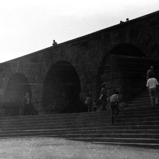People on steps beneath a stone archway structure.