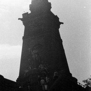 Monument with figures, people climbing stairs in grayscale.