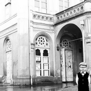 Boy stands near building in a flooded street.
