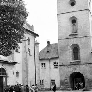 People gather outside a stone building with a tower.